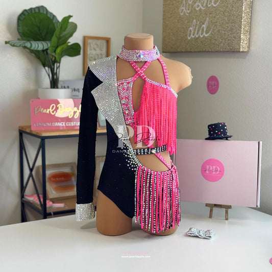 Hot pink and black jazz dance costume with rhinestone one-shoulder design, fringe detailing, and crystal choker displayed on a mannequin.
